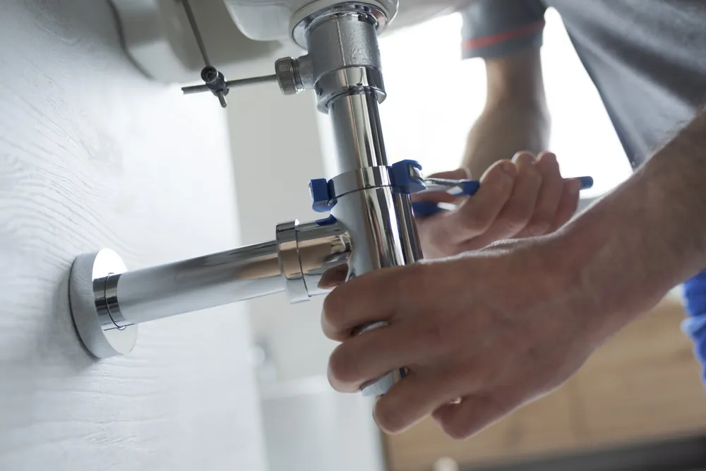Pacific Sheet Metal plumber fastening a pipe with a wrench.